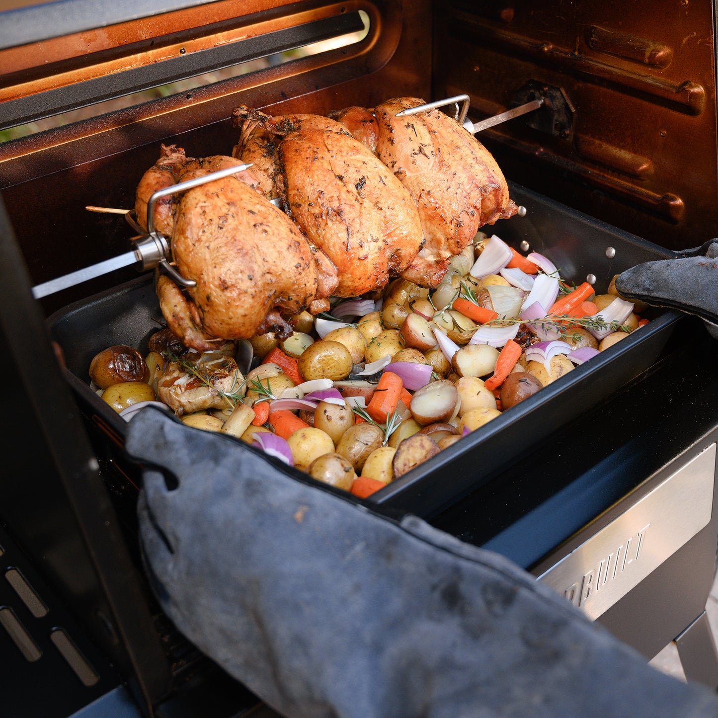 Three chickens cooking on a rotisserie BBQ.