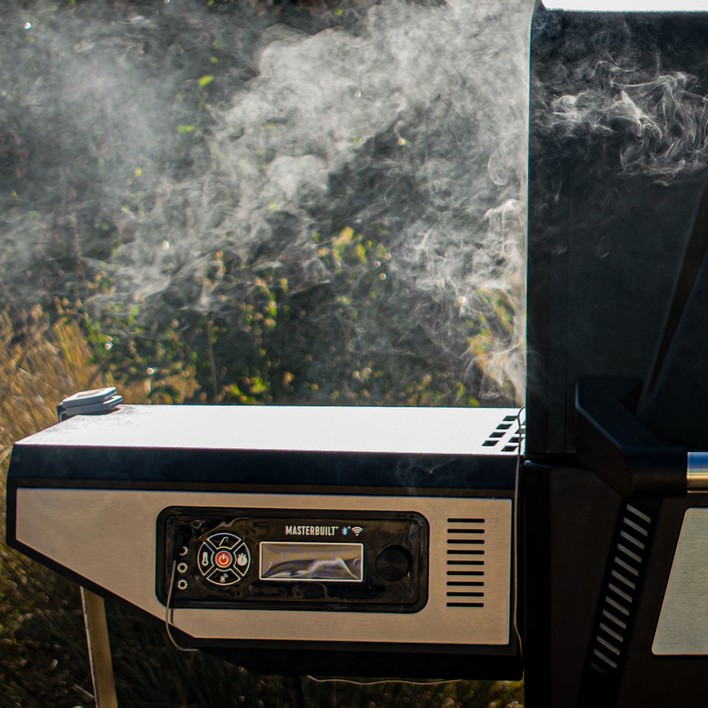 Portable grill with smoke rising from it, set against a natural background.