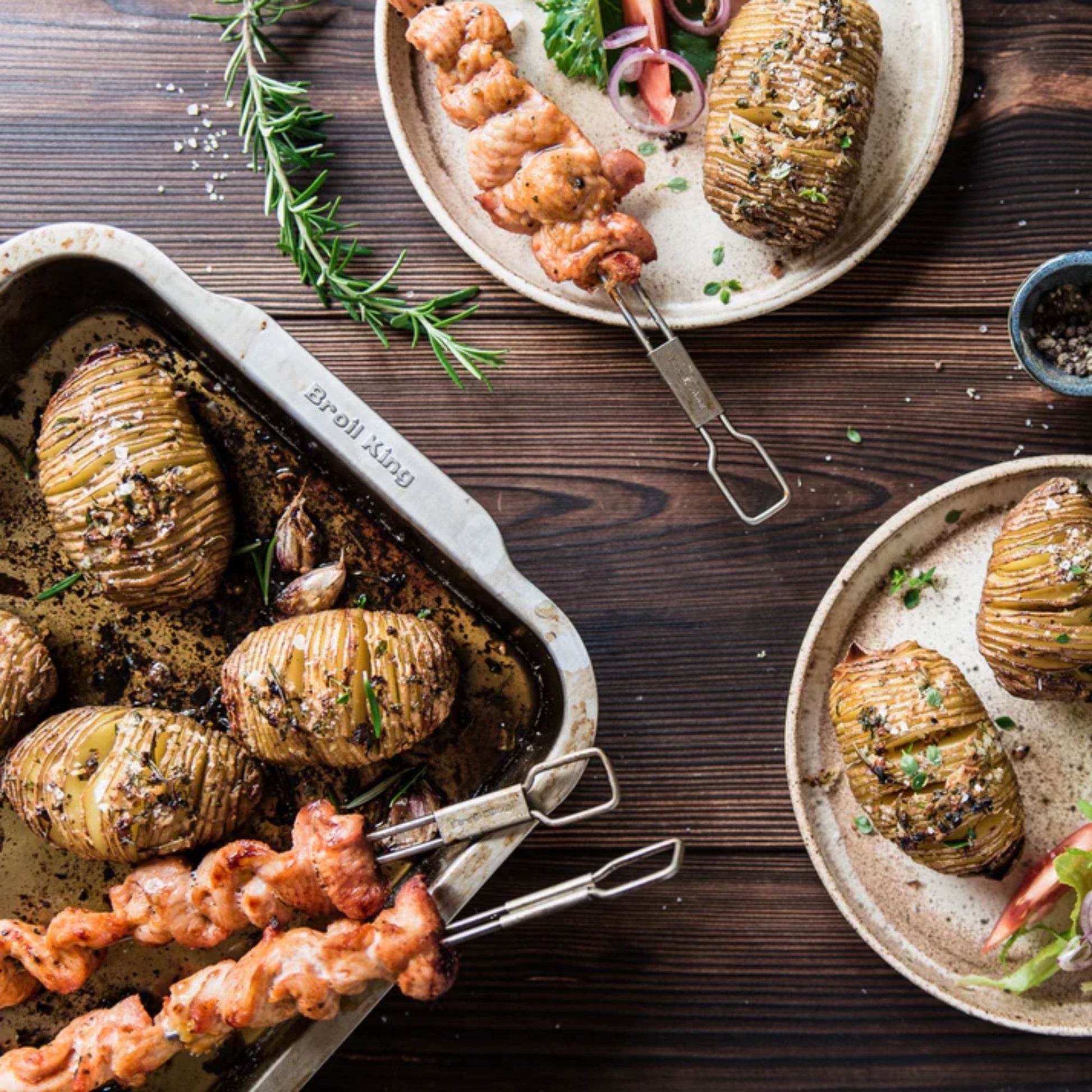 Hasselback potatoes on a wooden table with skewers and rosemary.