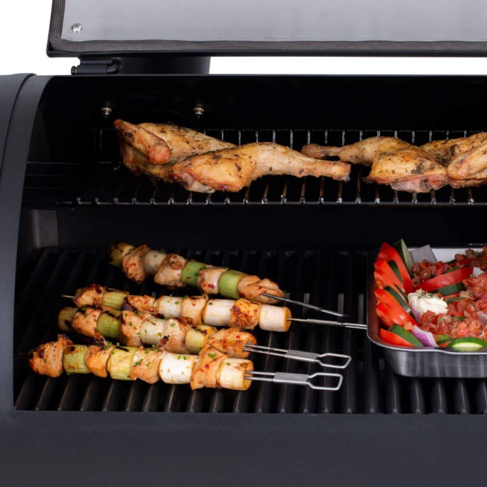 Grill with chicken, vegetable skewers, and a pan of vegetables cooking on it.