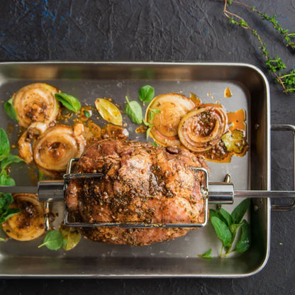 Roast beef on a rotisserie with onions and herbs on a dark surface