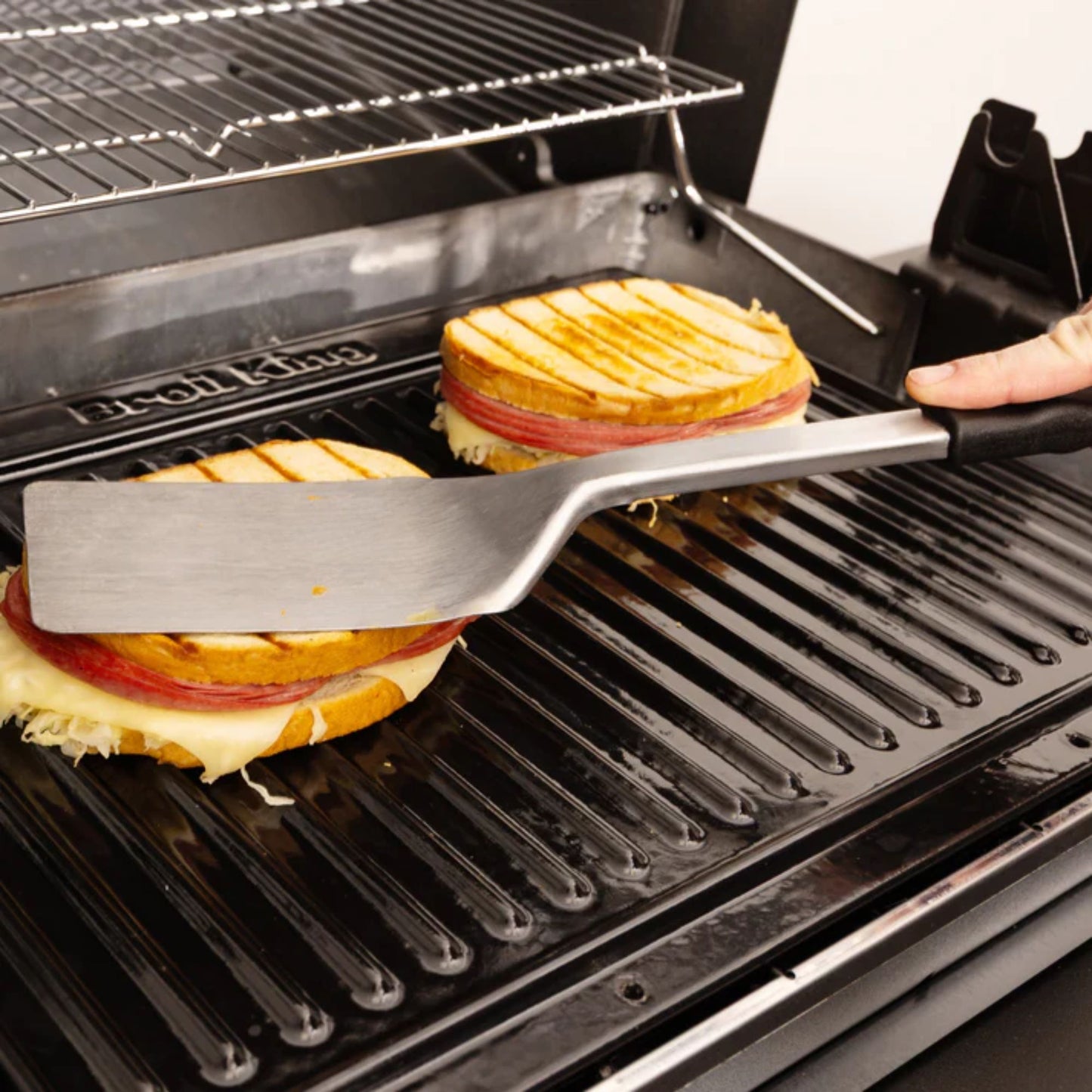 Grilled cheese sandwiches being prepared on a grill with tongs.