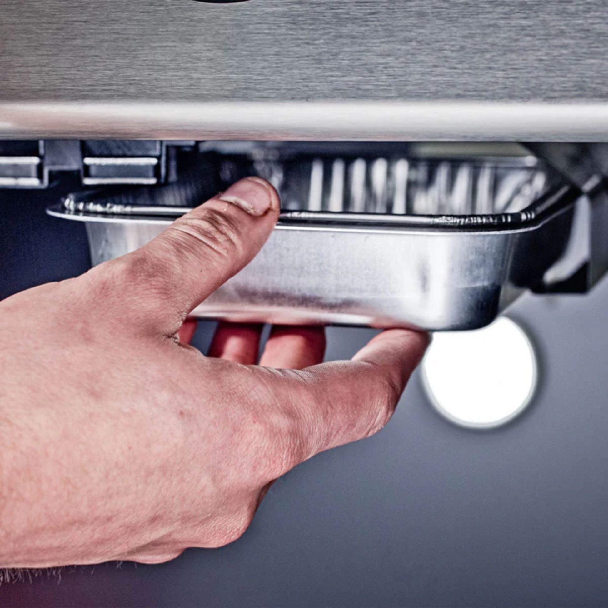 Hand fitting a foil tray in a BBQ.