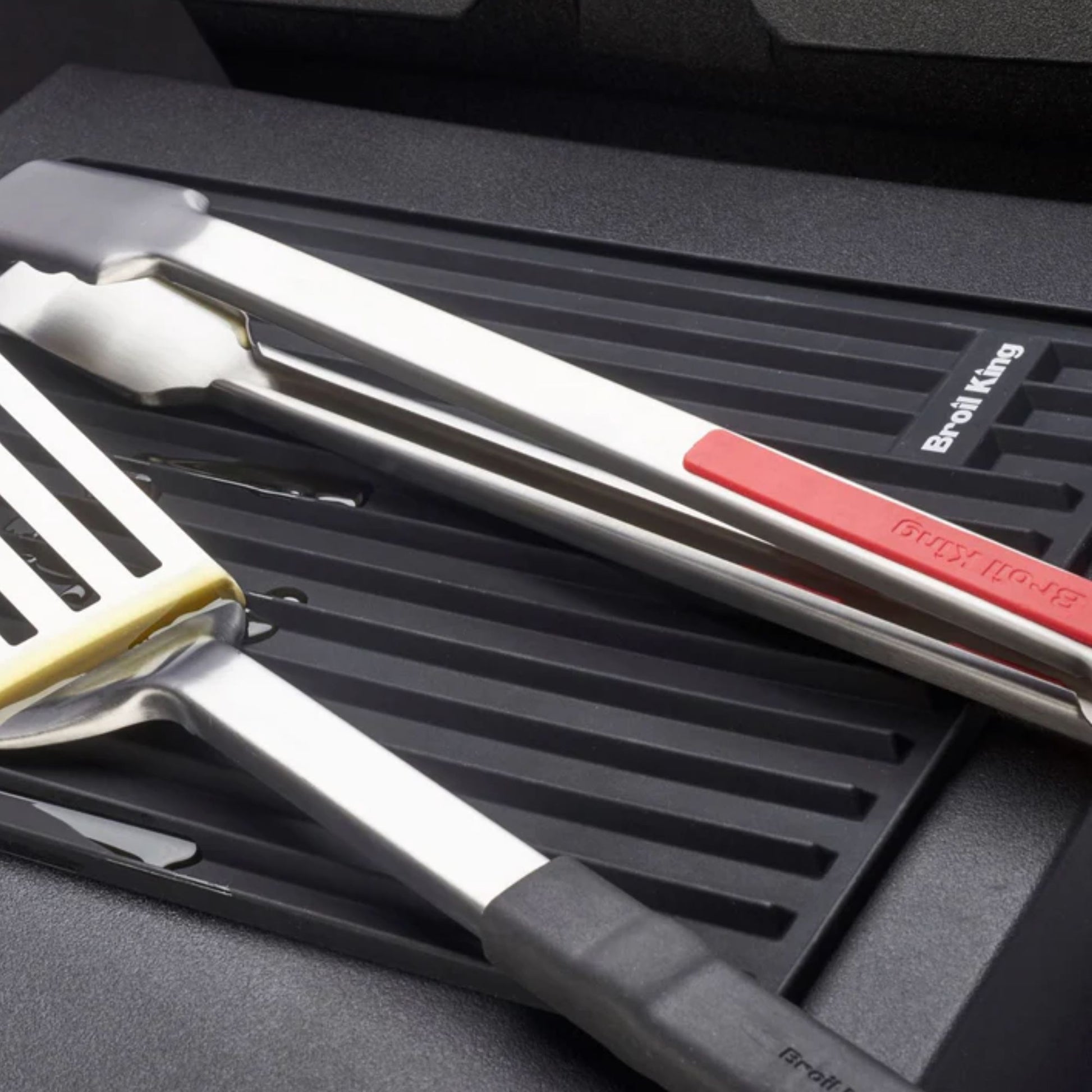 Barbecue tools including tongs and spatula in a silicone mat with brand name visible.