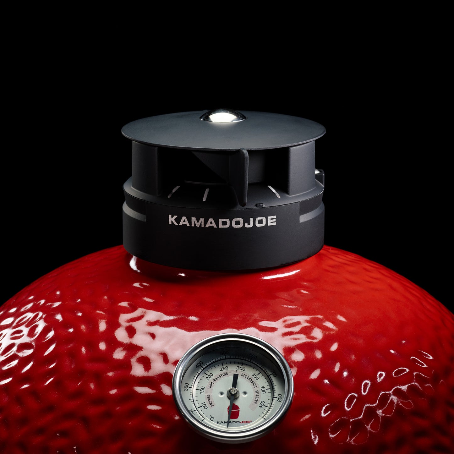 Red Kamado Joe grill with a black lid and thermometer on a black background