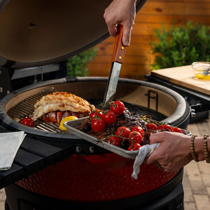 Person grilling vegetables and meat on a barbecue grill outdoors.