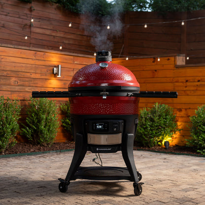 Red barbecue grill with smoke emitting from it, set against a wooden fence and outdoor setting.