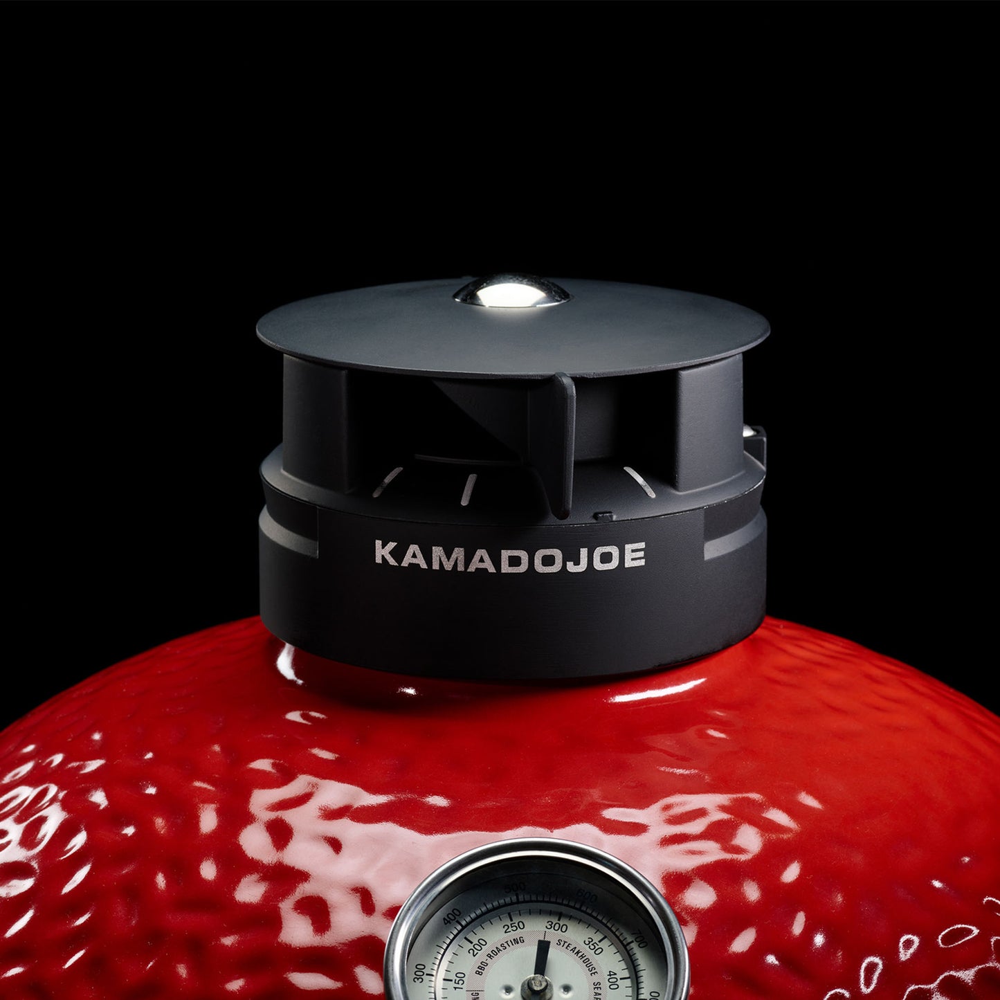 Red barbecue grill with a black Kamado Joe lid on a black background