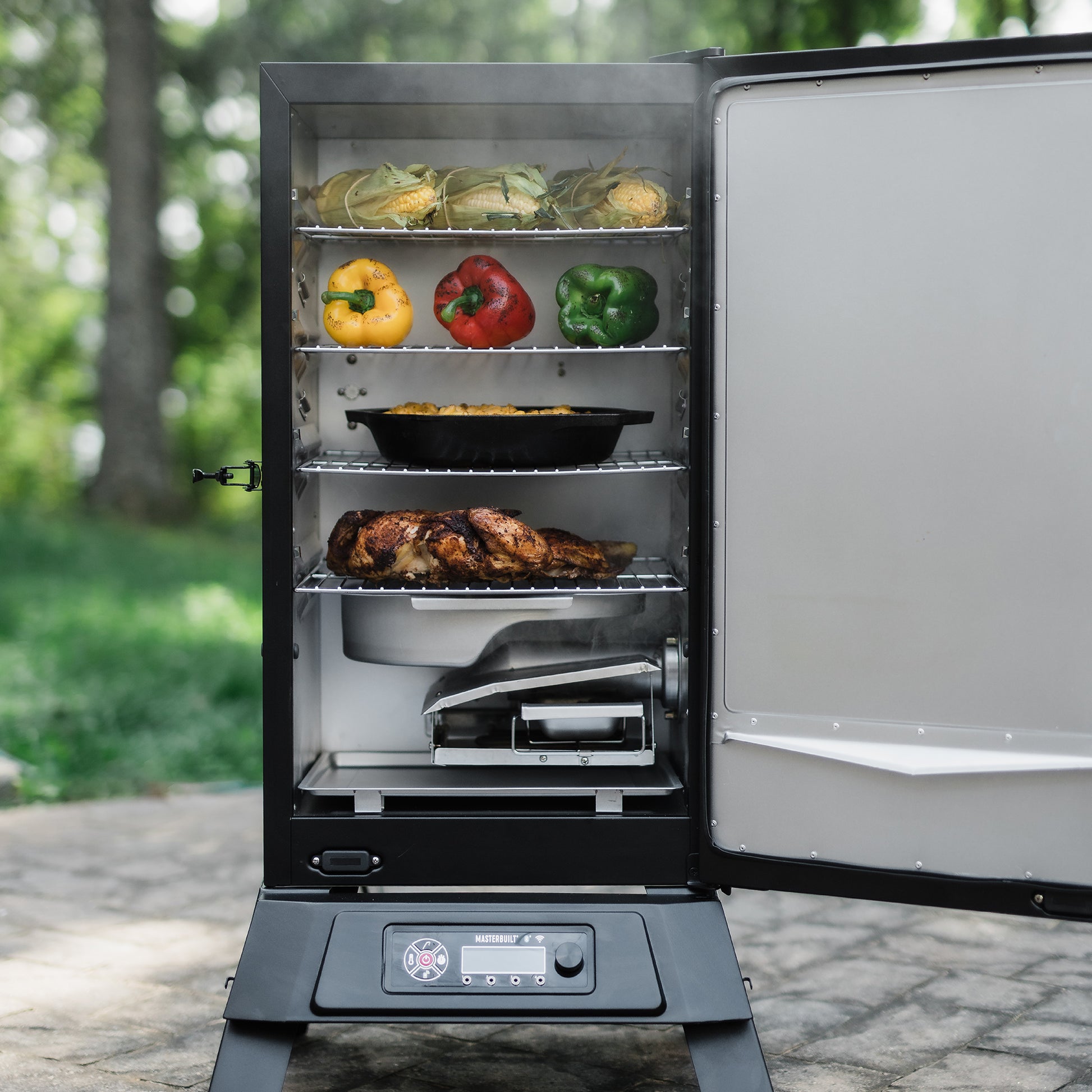 Smoker grill with food inside, including vegetables and a roasted chicken, outdoors.
