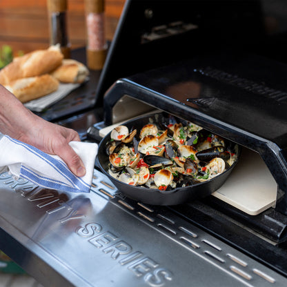 Person placing a pan of food into a portable stove with 'Masterbuilt' branding.