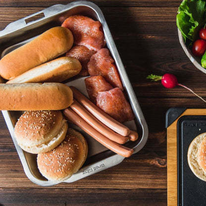Hot dogs and buns on a tray with a burger on a grill, on a wooden surface.