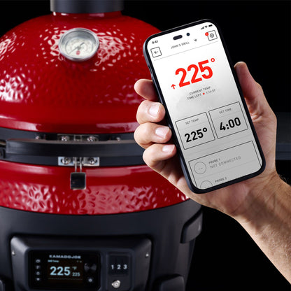 Red Kamado Joe grill with a hand holding a smartphone displaying a cooking app.