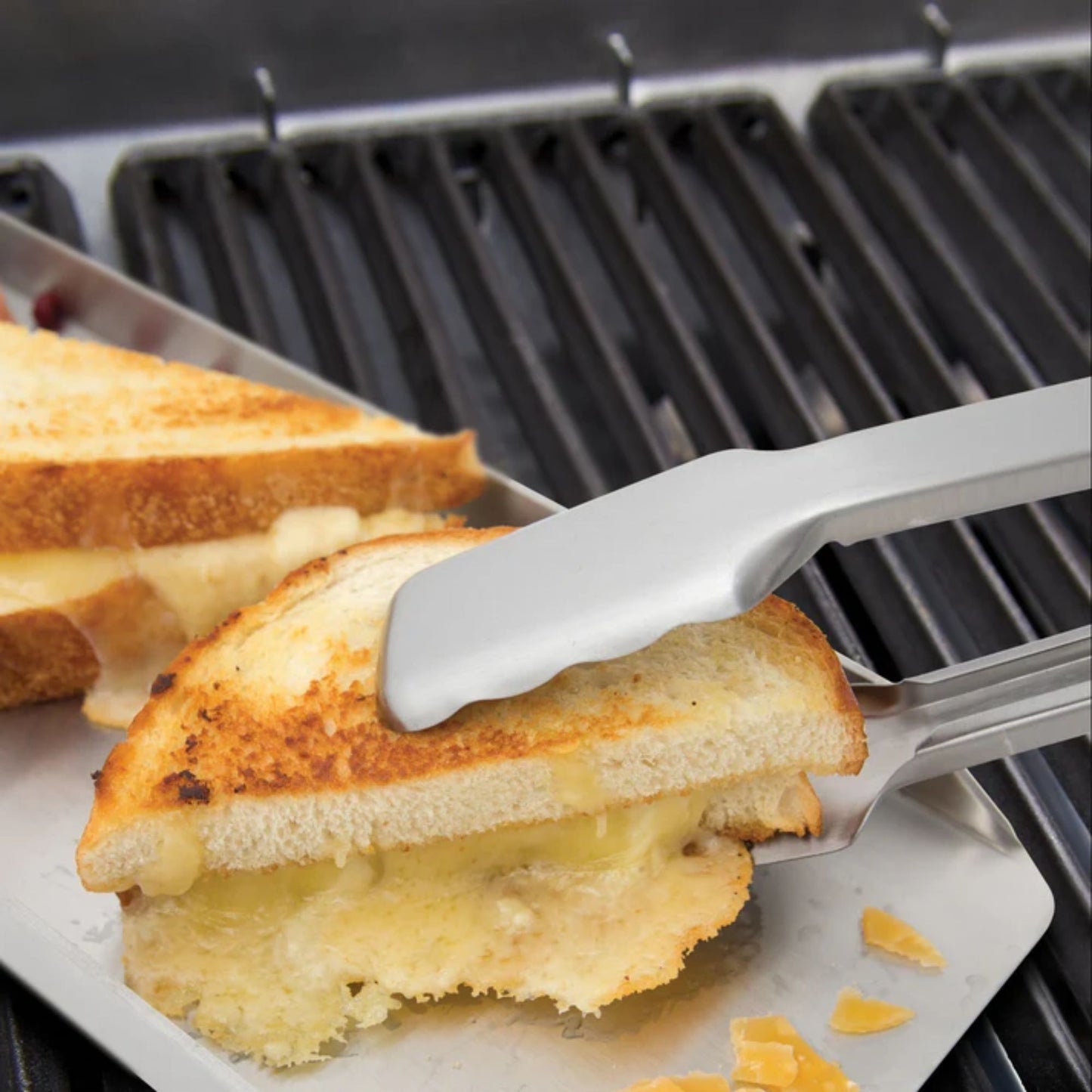 Grilled cheese sandwich being lifted with tongs on a grill
