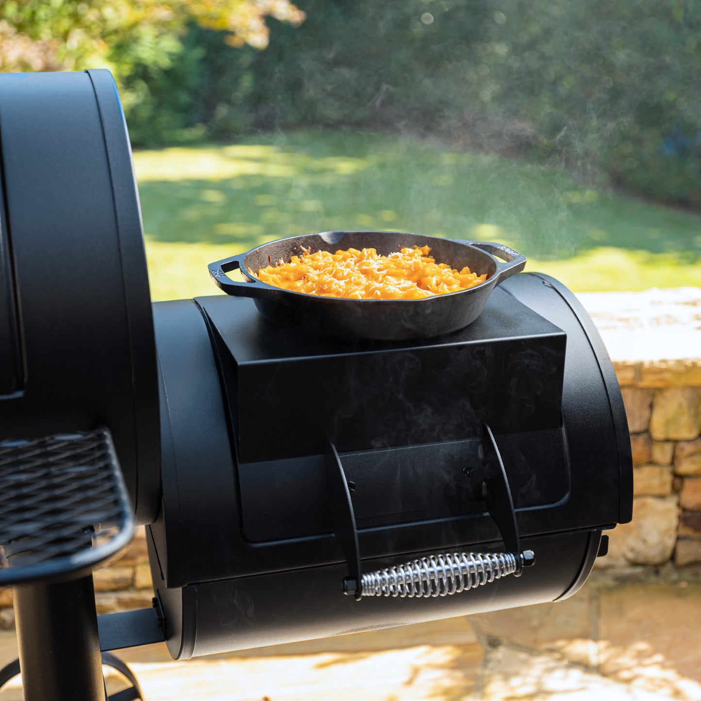 Black outdoor stove with a cast iron skillet containing food, set against a natural background.