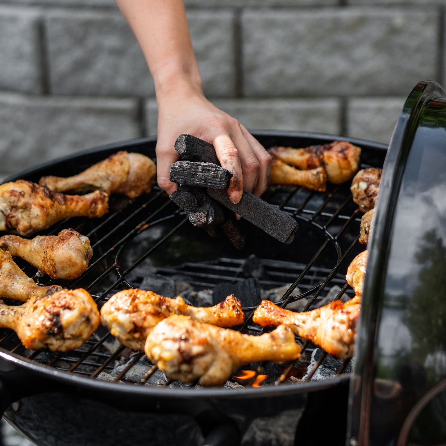 Person grilling chicken drumsticks on a barbecue grill with charcoal.