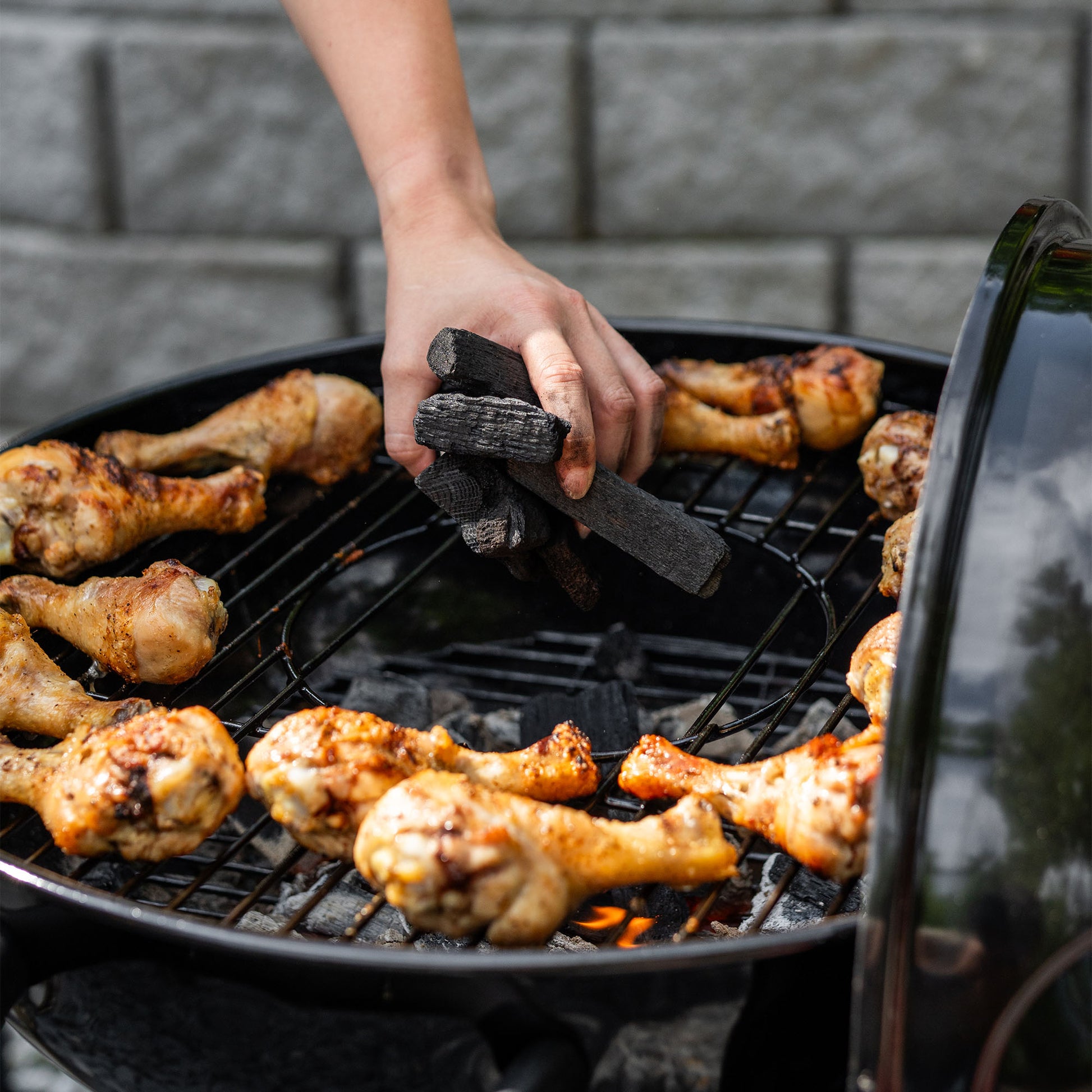 Person grilling chicken drumsticks on a barbecue grill with charcoal.