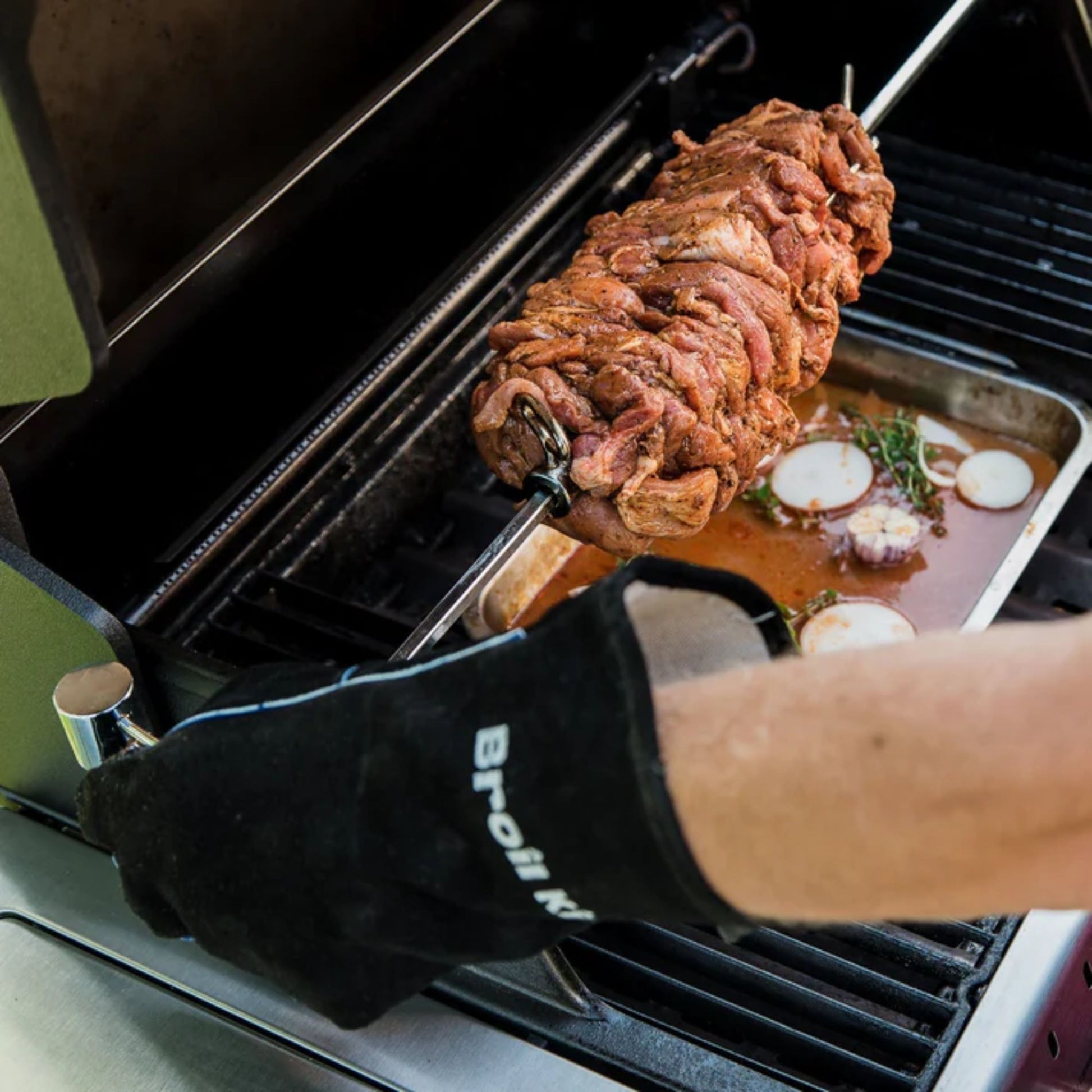 Person grilling a pork roast on a barbecue wearing Broil King leather gloves. 