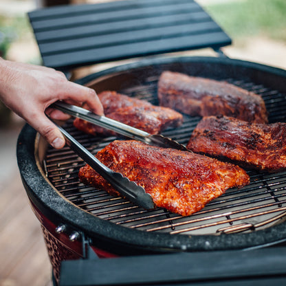 Person grilling ribs on a barbecue grill with tongs
