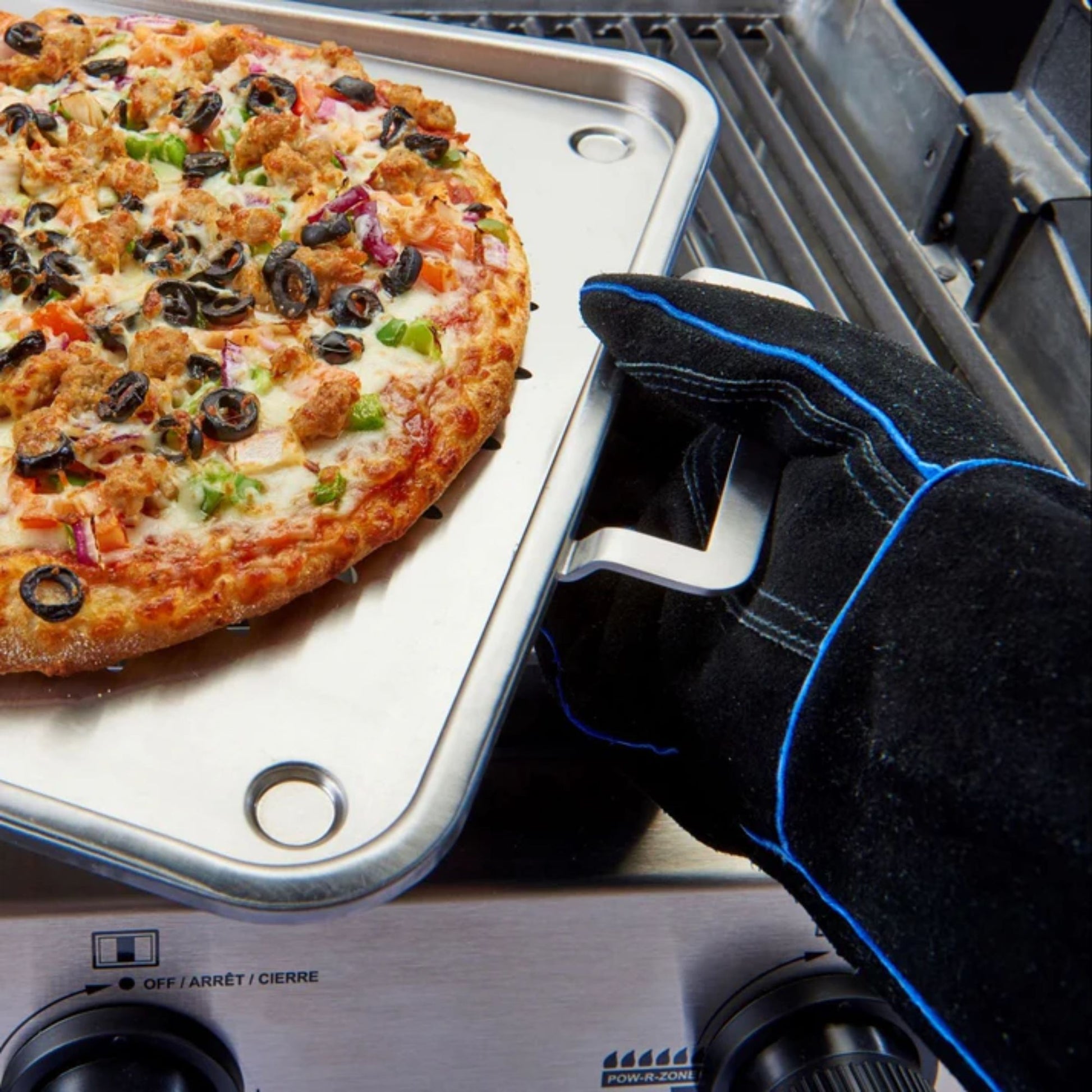 Person wearing an oven gloves reaching for a pizza on a portable stove.