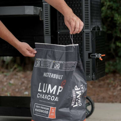 Person holding a bag of Masterbuilt lump charcoal in front of a grill.