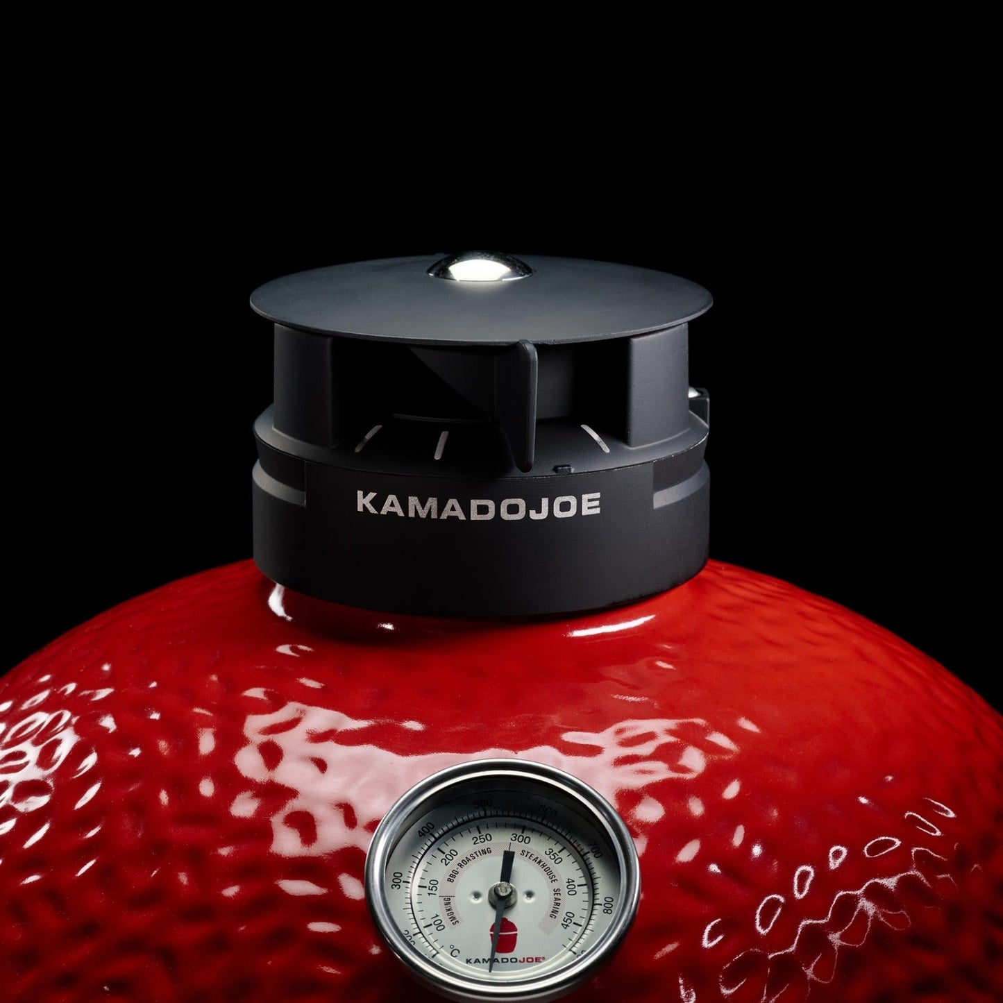 Red Kamado Joe grill with a black lid and thermometer on a black background
